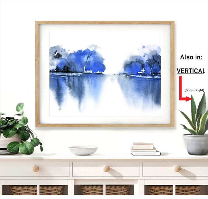 Op de afbeelding: Een ingelijst aquarel schilderij van een blauw en grijs landschap met bomen en een meer. Het schilderij is in een licht houten lijst en hangt aan een witte muur.