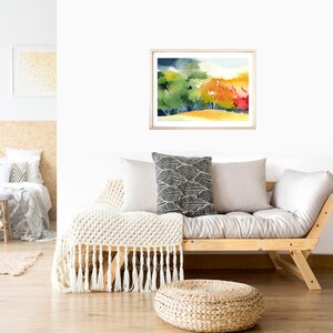 May include: A framed watercolor painting of a landscape with trees in shades of green, yellow, orange, and red. The trees are set against a background of a blue sky with white clouds.
