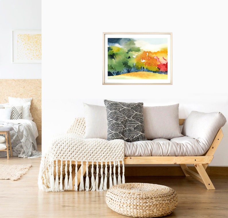 May include: A framed watercolor painting of a landscape with trees in shades of green, yellow, orange, and red. The trees are set against a background of a blue sky with white clouds.