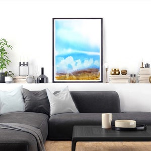 May include: A watercolor painting of a landscape with a blue sky, white clouds, and a field of golden grass. The painting is framed in a black frame and is hanging on a white wall.