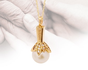May include: A gold-colored pendant necklace featuring a large, round, white pearl. The pendant has a rectangular top with the word "Mom" engraved on it, and a decorative, diamond-studded base. The necklace hangs from a delicate gold chain.