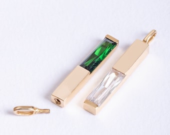 May include: Two gold pendants with a clear crystal and a green crystal. The pendants are shown next to a row of colored crystals representing each month of the year.