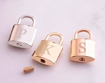 May include: Three personalized padlocks in silver, gold, and rose gold, each engraved with a single letter: P, K, and S. A small, gold-colored screw is placed near the padlocks.
