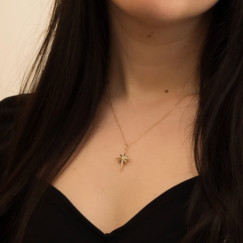 May include: A gold necklace with a star-shaped pendant. The necklace is worn by a person with long dark hair.
