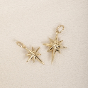 May include: Two gold star-shaped charms with a pointed design. The larger charm is slightly larger than the smaller charm.