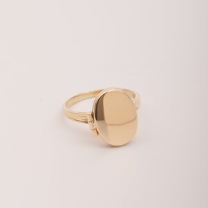 May include: A gold oval locket ring with a hinged opening. The ring is made of polished gold and has a smooth, shiny finish.