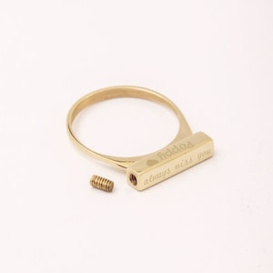 Könnte beinhalten: Goldring mit einem rechteckigen Balken, der mit "dad" und einem Herzsymbol sowie "always miss you" beschriftet ist. Der Ring ist offen und hat eine Schraube an der Seite.