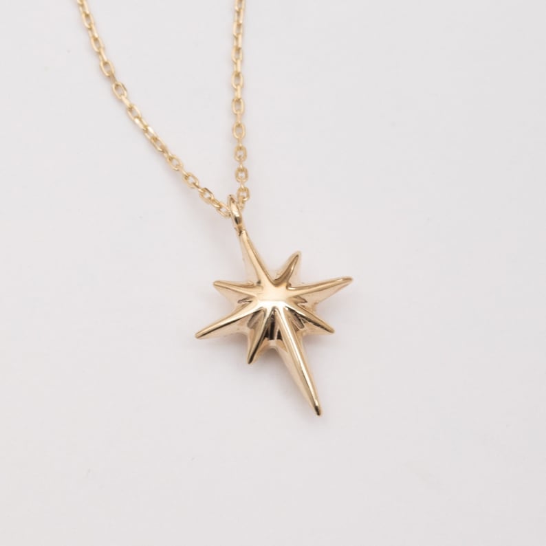 May include: A gold necklace with a star-shaped pendant. The star has a pointed design and is made of solid gold.