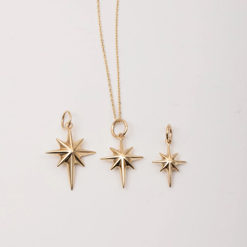May include: Three gold star-shaped pendants of different sizes. The largest pendant is on a gold chain.