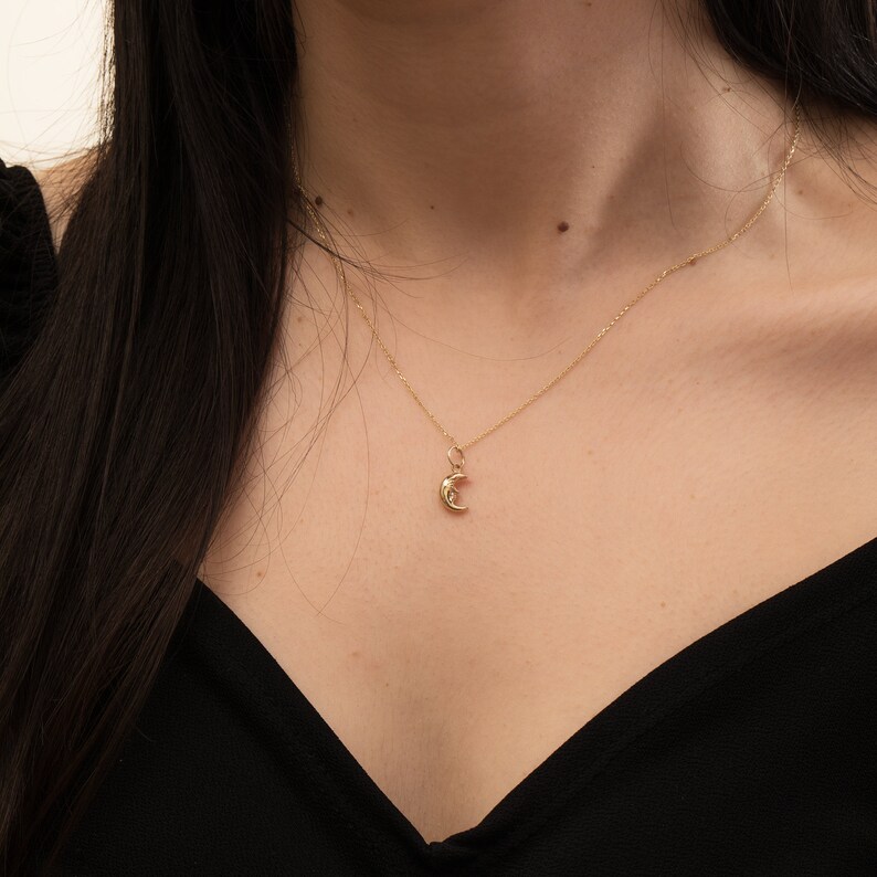 May include: A gold chain necklace with a crescent moon pendant.