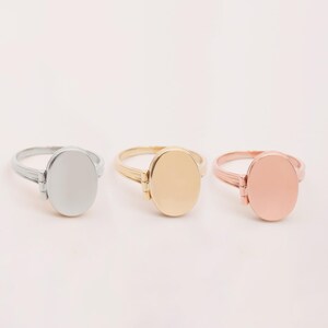 May include: Three oval locket rings in silver, gold, and rose gold. Each ring has a hinged lid that opens to reveal a small space for a photo or message.