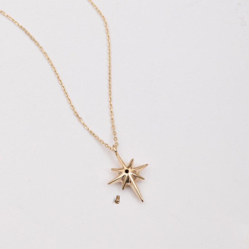 May include: A gold chain necklace with a star-shaped pendant. The pendant has a small hole in the center and is attached to the chain with a small screw.