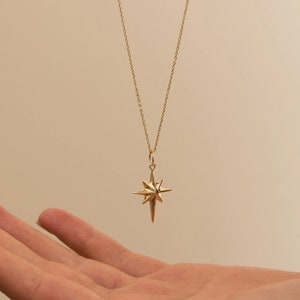 May include: A gold chain necklace with a star-shaped pendant. The star has a pointed design and is made of gold metal.