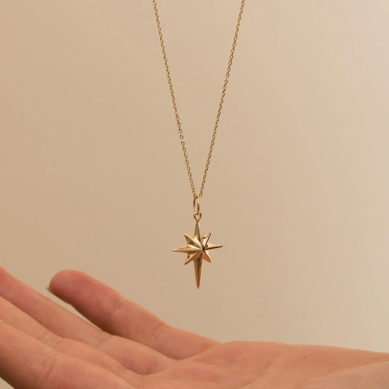 May include: A gold chain necklace with a star-shaped pendant. The star has a pointed design and is made of gold metal.