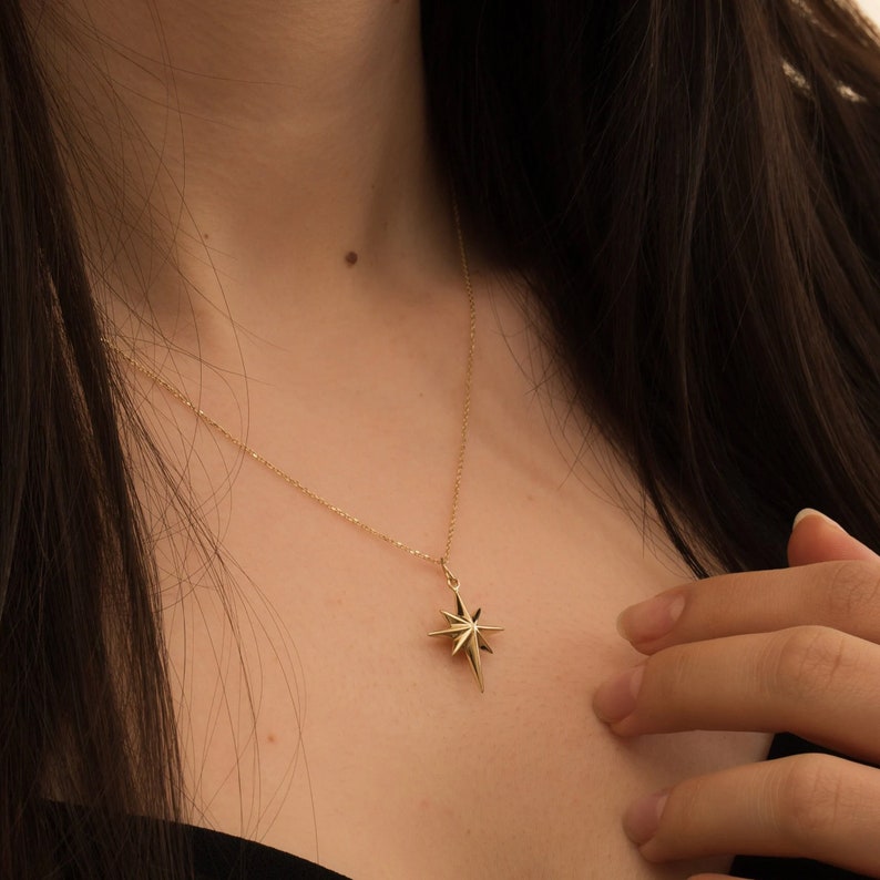 May include: A gold necklace with a star-shaped pendant. The star has a pointed design and is made of a shiny metal.