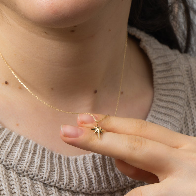 May include: A gold chain necklace with a star-shaped pendant. The pendant is a simple, geometric design with a pointed tip.