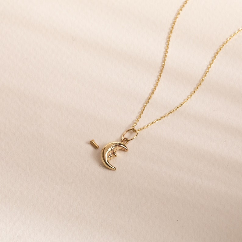 May include: A gold chain necklace with a crescent moon charm. The charm is detailed with a face and a small star.