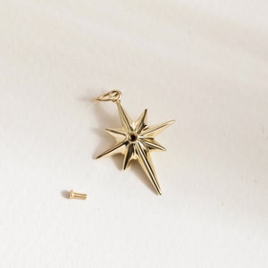 May include: A gold-toned star-shaped pendant with a small hole in the center. The pendant is attached to a gold-toned chain.