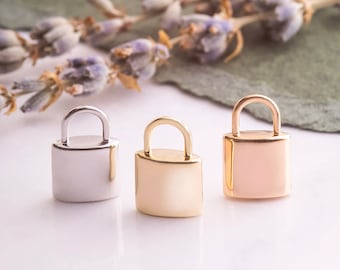 May include: Three small lock charms in silver, gold, and rose gold. The charms are in the shape of padlocks with a rounded top and a flat bottom.