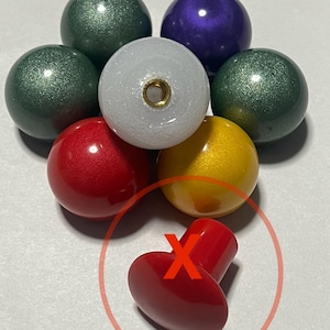 May include: A collection of seven colorful round knobs with a red knob on a white surface. The round knobs are in various colors including green, purple, white, red, and yellow.