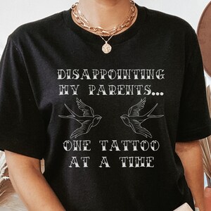 May include: Black t-shirt with the text "DISAPPOINTING MY PARENTS... ONE TATTOO AT A TIME" and two stylized birds.