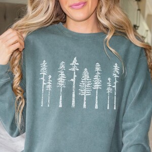 Könnte beinhalten: Ein blaugrünes Sweatshirt mit einer weißen Grafik einer Reihe von stilisierten Bäumen. Die Bäume sind im Vintage-Stil mit einem Used-Look.