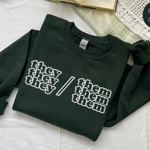 May include: Forest green sweatshirt with the text "they/them" printed in white.