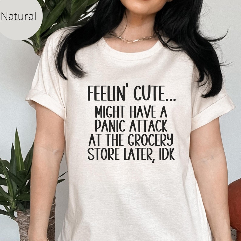 May include: A white t-shirt with black text that reads "Feelin' Cute... Might Have A Panic Attack At The Grocery Store Later, IDK."
