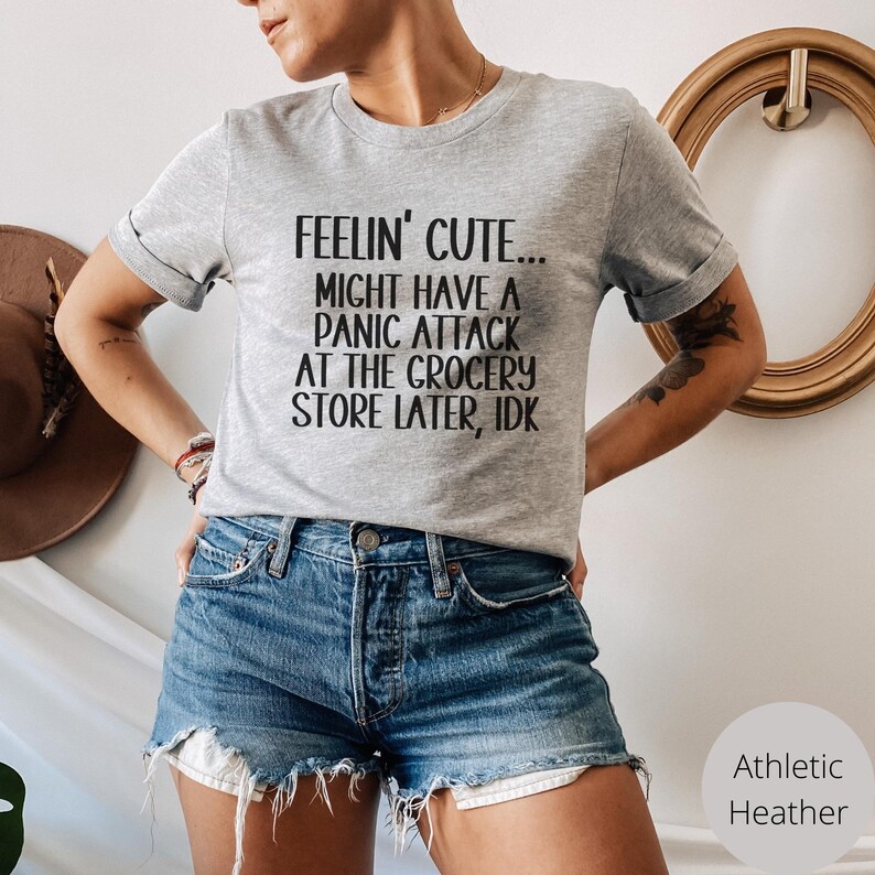 May include: A grey t-shirt with the text "Feelin' Cute... Might have a panic attack at the grocery store later, idk" printed in black.