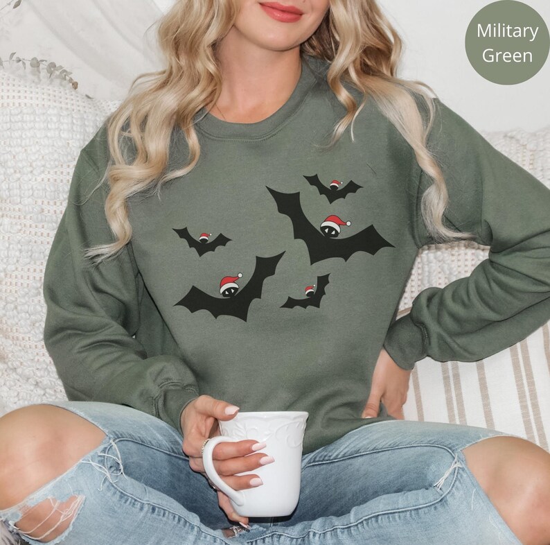 K&ouml;nnte beinhalten: Ein gr&uuml;nes Sweatshirt mit einem Weihnachts-Fledermaus-Design. Die Flederm&auml;use tragen Weihnachtsm&uuml;tzen und fliegen in einer Gruppe. Das Sweatshirt ist bequem und l&auml;ssig.