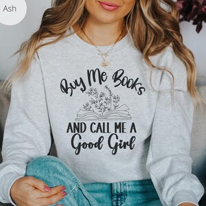 May include: A gray sweatshirt with the text "Buy Me Books and Call Me a Good Girl" printed on it. The text is surrounded by a drawing of an open book with flowers.