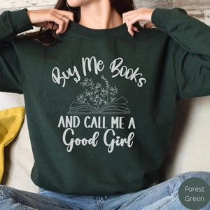 May include: A dark green sweatshirt with the text "Buy Me Books and Call Me a Good Girl" in white lettering. The text is surrounded by a stylized image of an open book with flowers.