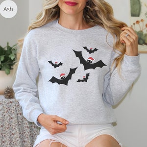 K&ouml;nnte beinhalten: Ein graues Sweatshirt mit einem weihnachtlichen Design mit schwarzen Flederm&auml;usen, die Weihnachtsm&uuml;tzen tragen. Die Flederm&auml;use fliegen in verschiedene Richtungen.