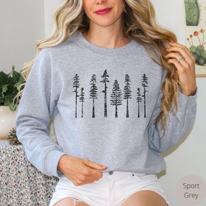 May include: A grey sweatshirt with a black print of a row of trees. The trees are stylized and have a distressed look. The sweatshirt is a crew neck style with long sleeves.