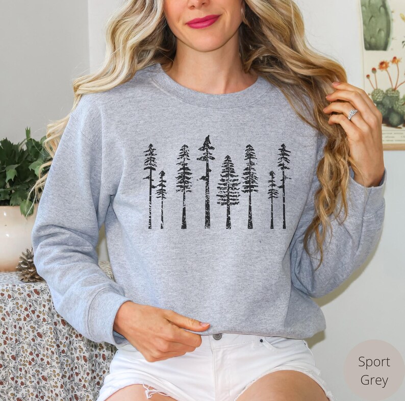 May include: A grey sweatshirt with a black print of a row of trees. The trees are stylized and have a distressed look. The sweatshirt is a crew neck style with long sleeves.