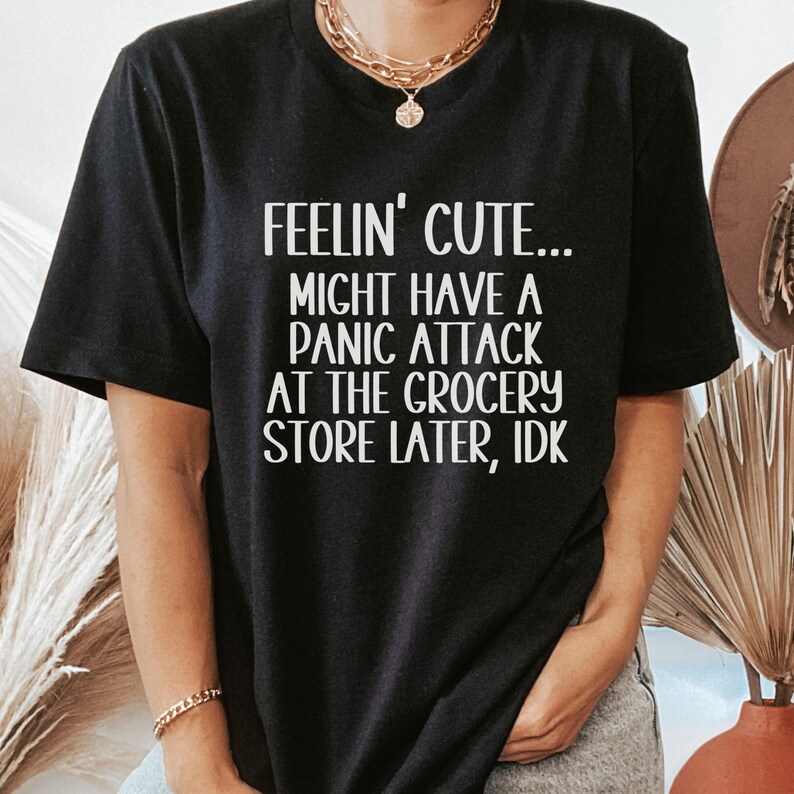 May include: Black t-shirt with white text that reads "Feelin' cute... Might have a panic attack at the grocery store later, idk."