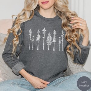 May include: A dark heather grey sweatshirt with a white graphic of a row of stylized trees.