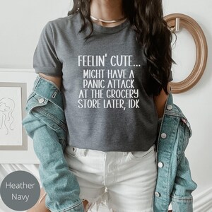 May include: A dark heather grey t-shirt with white text that reads "Feelin' Cute... Might have a panic attack at the grocery store later, idk."