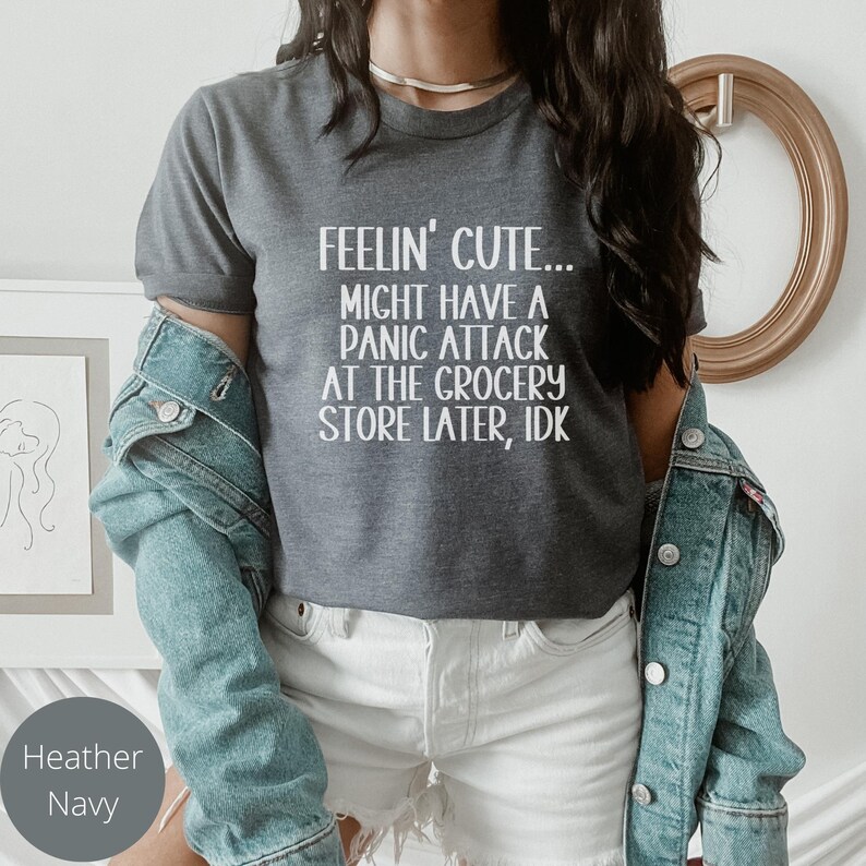 May include: A dark heather grey t-shirt with white text that reads "Feelin' Cute... Might have a panic attack at the grocery store later, idk."