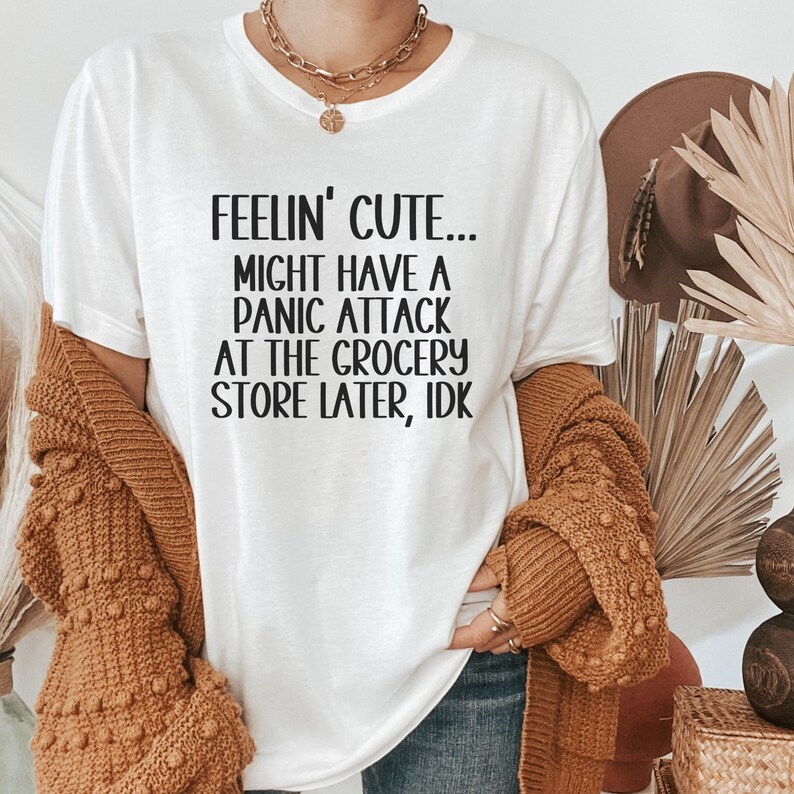 May include: White t-shirt with black text that reads "Feelin' Cute... Might Have A Panic Attack At The Grocery Store Later, IDK"