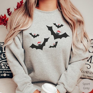 K&ouml;nnte beinhalten: Ein graues Sweatshirt mit einem schwarzen und roten Design von Flederm&auml;usen, die Weihnachtsm&uuml;tzen tragen. Das Sweatshirt hei&szlig;t "Sport Grey".