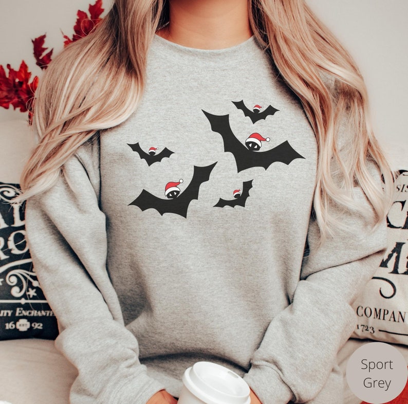 K&ouml;nnte beinhalten: Ein graues Sweatshirt mit einem schwarzen und roten Design von Flederm&auml;usen, die Weihnachtsm&uuml;tzen tragen. Das Sweatshirt hei&szlig;t "Sport Grey".