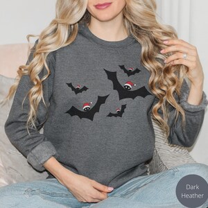 K&ouml;nnte beinhalten: Ein dunkel-helles graues Sweatshirt mit einem festlichen Design von Flederm&auml;usen, die Weihnachtsm&uuml;tzen tragen.