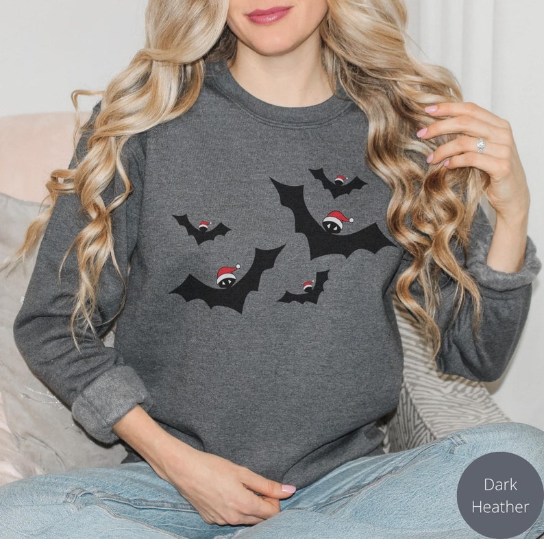 K&ouml;nnte beinhalten: Ein dunkel-helles graues Sweatshirt mit einem festlichen Design von Flederm&auml;usen, die Weihnachtsm&uuml;tzen tragen.
