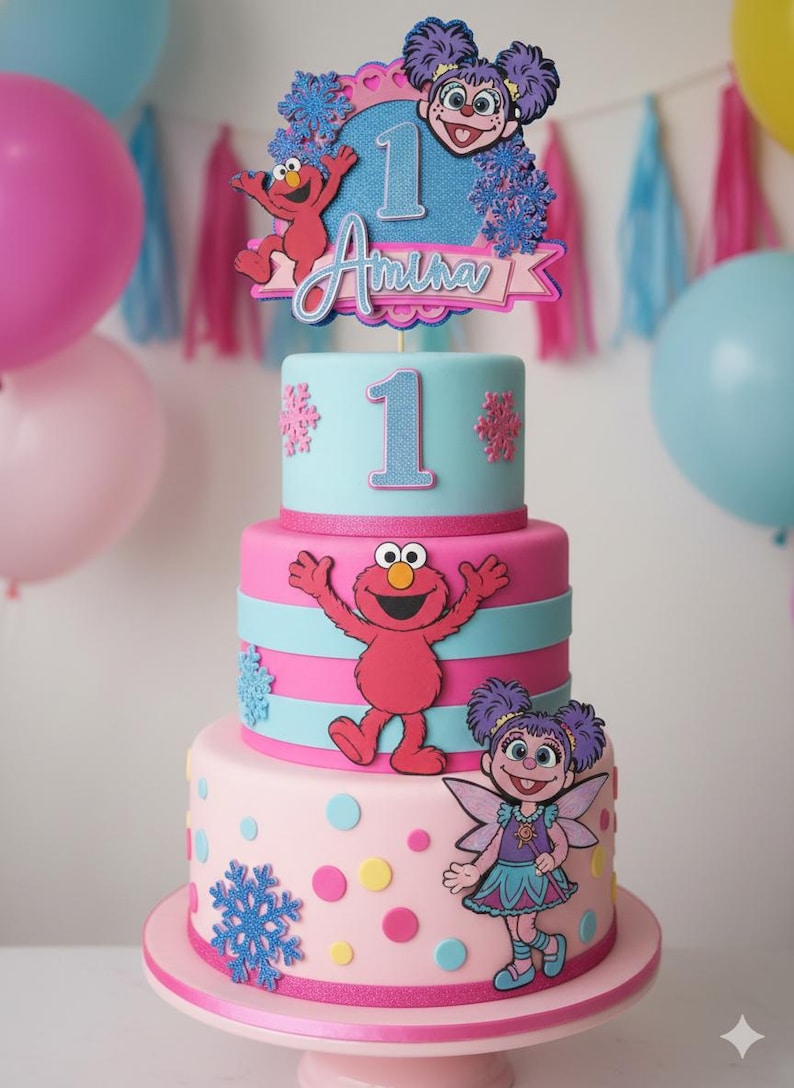 May include: A three-tiered birthday cake with pink, blue, and white frosting. The cake is decorated with Sesame Street characters, snowflakes, and the name "Amina" with the number "1". The cake sits on a pink cake stand.