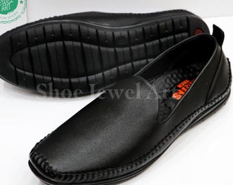 May include: Black leather slip-on shoes with stitched detailing. The shoes have a textured rubber sole for grip and comfort. The image shows the top and bottom of the shoes, highlighting their design and construction. The shoes are a classic style.