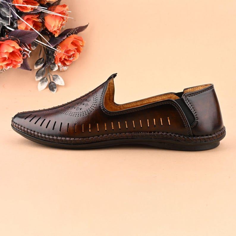 May include: Brown leather slip-on shoe with decorative perforations and cut-out design. The shoe features a rounded toe and a dark brown sole. The shoe is a classic style, suitable for casual or semi-formal wear.