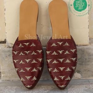 May include: A pair of burgundy leather slip-on shoes with a pointed toe. The shoes feature a light brown insole and are decorated with embroidered floral patterns in a lighter shade. The text "Shoe Jewel Art" is visible on the shoes.