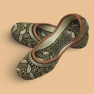 May include: A pair of olive green embroidered flats with a floral design. The shoes have a brown leather trim and a cream-colored interior. The embroidery is in a cream color, creating a contrast against the green fabric.