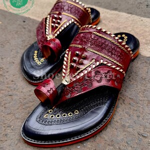 Puede incluir: Un par de sandalias de cuero hechas a mano. Las sandalias presentan una parte superior de cuero rojo oscuro con intrincados patrones florales en relieve y costuras doradas. Las suelas son negras con ribete rojo y ojales dorados. C&oacute;modas y elegantes.
